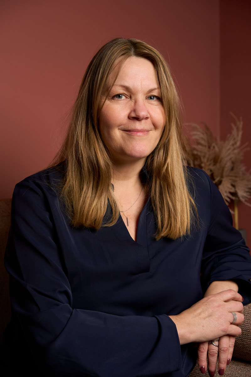Portrait corporate naturel d'une consultante blonde souriante en chemisier bleu marine sur fond terracotta, shooting équipe Paris