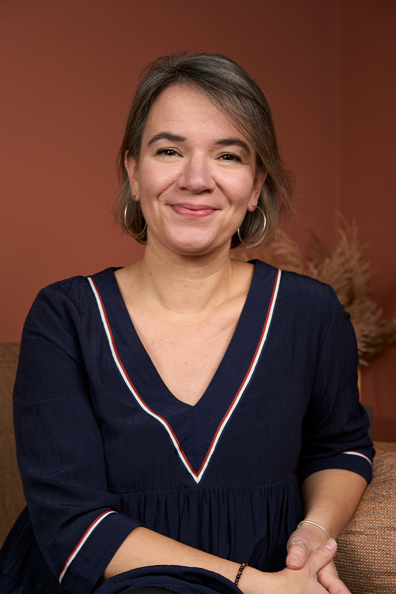 Portrait corporate naturel d'une formatrice en robe bleu marine à col V sur fond terracotta, shooting équipe Paris