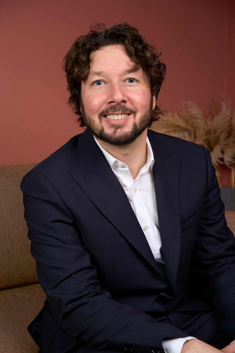 Portrait corporate d'un consultant souriant en costume bleu sur fond terracotta, cabinet de conseil Paris